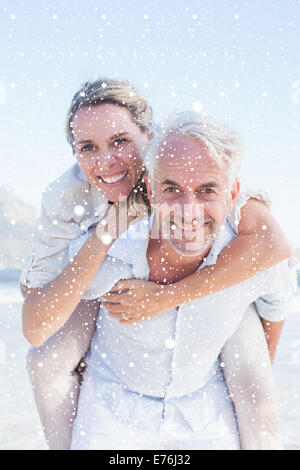 Immagine composita dell'uomo dando la sua moglie sorridente una piggy back in spiaggia Foto Stock