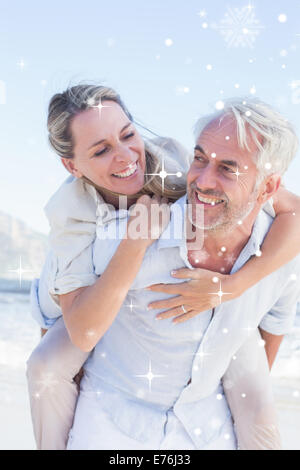 Immagine composita dell'uomo dando la sua moglie sorridente una piggy back in spiaggia Foto Stock