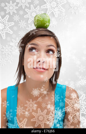 Immagine composita di attraente giovane donna in posizione eretta con una mela verde sul suo capo Foto Stock