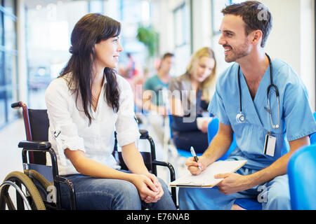 Paziente in carrozzella parlando a un infermiere in ospedale Foto Stock