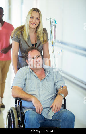 Donna wheeling padre in ospedale in corridoio Foto Stock