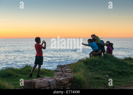 Ragazzo prende una foto dei suoi amici al tramonto sulla costa a sud di Città del Capo, Sud Africa Foto Stock