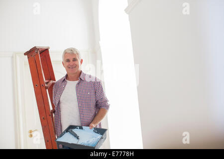 Vecchio uomo che porta la scaletta e vassoio di vernice Foto Stock