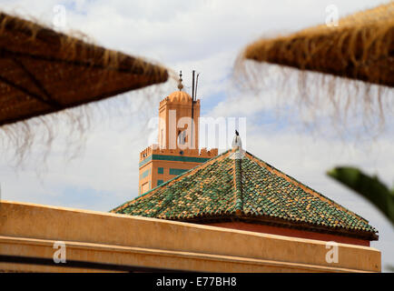 Tetti in Medina o la vecchia città di Marrakech con piastrelle verdi e un piccione, ombrelloni e il minareto della moschea Foto Stock