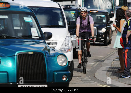 Un ciclista in bicicletta a Londra tra una coda di traffico. Pedoni in attesa di attraversare la strada Foto Stock