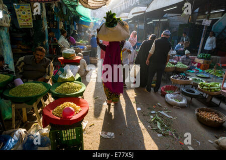 Una donna sta portando un sacchetto con le verdure sul suo capo attraverso il mercato ortofrutticolo, Ahmedabad, Gujarat, India Foto Stock