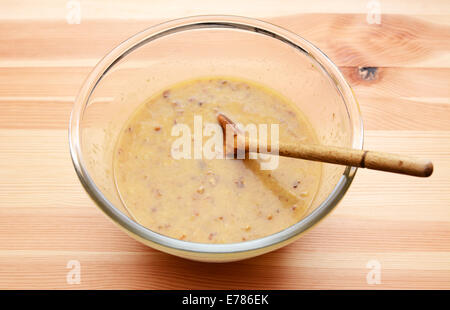 Banana focaccia ingredienti umidi - purea di frutta, uova, burro - in una ciotola di vetro con un cucchiaio di legno Foto Stock