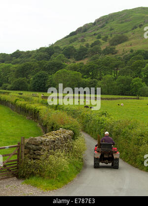 Inglese paesaggio rurale con il contadino su quad bike guida sulla stretta strada fiancheggiata da siepi e circondata da verdi campi e colline Foto Stock