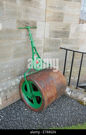 Il vecchio rullo di prato con metallo arrugginito tamburo / rullo e verde maniglia verniciata appoggiata contro la parete Foto Stock