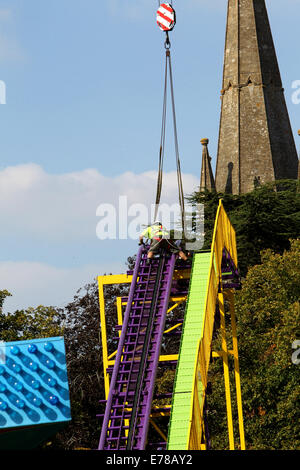 Witney, Oxfordshire, Regno Unito, 9 settembre 2014. Fiera dei lavoratori utilizzare una gru per impostare un rollercoaster ride in blazing sunshine in preparazione per la festa di Witney questo fine settimana. La festa annuale di Santa Maria è stato tenuto dal 1243 per commemorare il re-dedicazione della chiesa di Santa Maria quando il Vescovo ha dato un cervo al rettore di modo che la gente della città potrebbe festeggiare l'occasione. Oggi un arrosto di maiale sulla Chiesa ancora verde segna questa parte della tradizione accanto alle giostre e baracconi, chioschi, musica ed eventi sportivi Credito: Ric Mellis/Alamy Live News Foto Stock