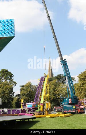 Witney, Oxfordshire, Regno Unito, 9 settembre 2014. Fiera dei lavoratori utilizzare una gru per impostare un rollercoaster ride in blazing sunshine in preparazione per la festa di Witney questo fine settimana. La festa annuale di Santa Maria è stato tenuto dal 1243 per commemorare il re-dedicazione della chiesa di Santa Maria quando il Vescovo ha dato un cervo al rettore di modo che la gente della città potrebbe festeggiare l'occasione. Oggi un arrosto di maiale sulla Chiesa ancora verde segna questa parte della tradizione accanto alle giostre e baracconi, chioschi, musica ed eventi sportivi Credito: Ric Mellis/Alamy Live News Foto Stock