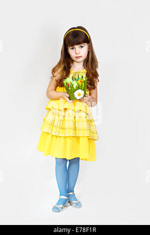 Carino bambina in giallo pone con nido di pasqua in mani. Ful altezza verticale sul naturale sfondo grigio Foto Stock