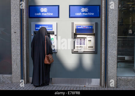 Una donna in burka usando un Halifax bancomat Foto Stock