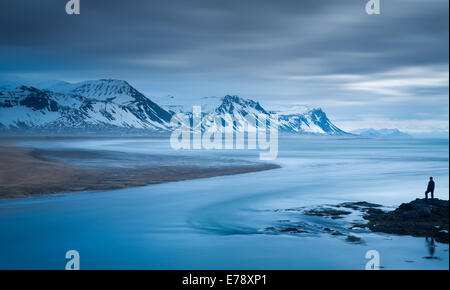 La figura solitaria di Wendy sulla costa a Budir con montagne di Holsfjall e la penisola di Snaefellsnes western Islanda Foto Stock