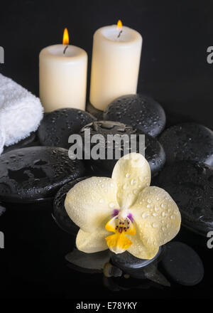 Bellissima spa set di orchidea gialla (phalaenopsis), ZEN pietre con gocce, candele e impilati asciugamani su acqua di riflessione Foto Stock