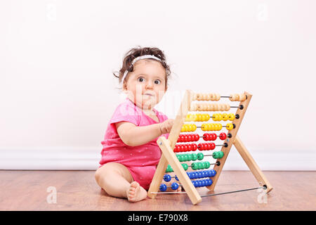 Bambina gioca con un abaco seduto sul pavimento in legno Foto Stock