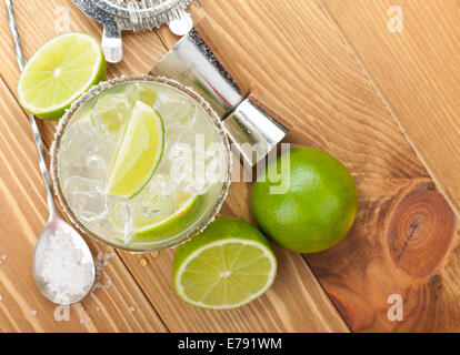 Classico cocktail Margarita con il salato cerchione sulla tavola di legno con tigli e bere utensili Foto Stock