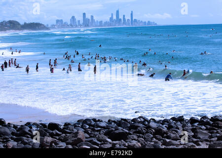 Surfers godendo le onde a Burleigh capi sulla Gold Coast in Australia. Surfers Paradise è in distanza. Foto Stock