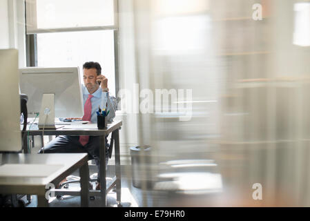 Un uomo seduto allo schermo di un computer al lavoro sul suo proprio. Foto Stock