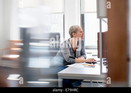 Una donna che lavora in un ufficio alla sua scrivania, utilizzando un mouse del computer. Foto Stock