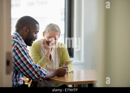 Un uomo e una donna in un ufficio, la condivisione di una tavoletta digitale. Foto Stock