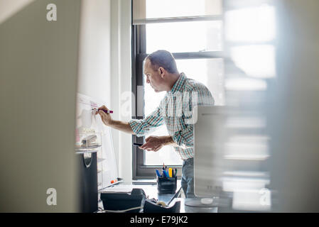 Vita in ufficio. Un uomo in piedi fino a lavorare e a rendere note su un tabellone a parete. Gestione di progetto. Foto Stock