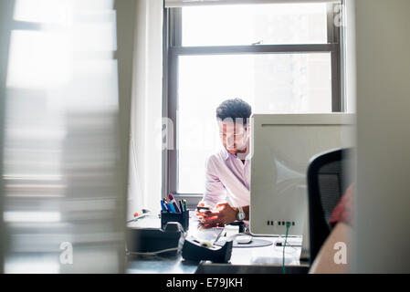 Vita in ufficio. Un uomo di controllare il suo telefono in un ufficio. Foto Stock