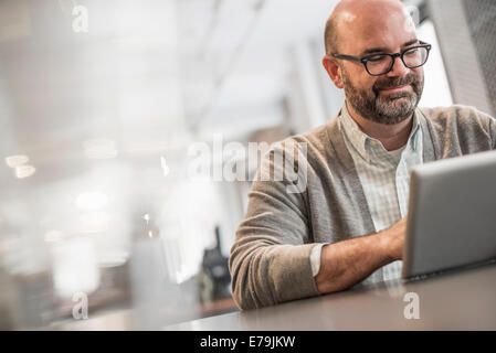 Vita in ufficio. Un uomo seduto al tavolo, per lavorare su un computer portatile. Foto Stock