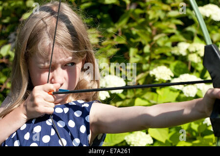 Piccola ragazza caucasica freccia di puntamento dal grande arco all'aperto sullo sfondo della natura Foto Stock