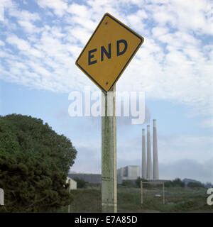 Un dead end road sign in primo piano, fumo pile emettendo fumo in background Foto Stock