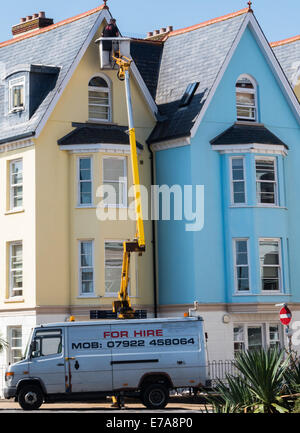 Teignmouth, Devon, Inghilterra. Un uomo su un cherry picker pittura 4 storie su di un lato di un edificio. Foto Stock