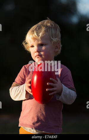 Carino Ragazzo che guarda lontano mentre si tiene un calcio al di fuori Foto Stock