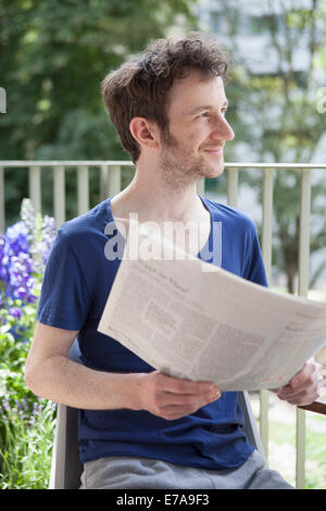 Giovane uomo che guarda lontano tenendo quotidiano a portico Foto Stock