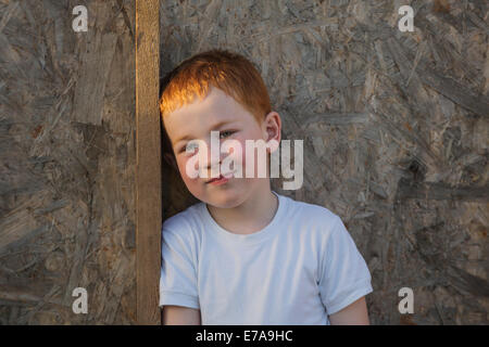 Ritratto di giovane ragazzo appoggiato sulla tavola in legno Foto Stock