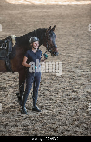 Per tutta la lunghezza della donna in piedi con il cavallo in stabile di formazione Foto Stock