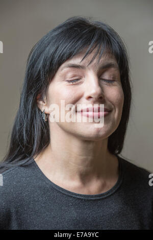 Sorridente donna matura con gli occhi chiusi contro uno sfondo grigio Foto Stock