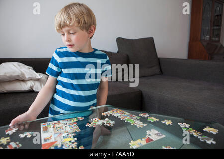 Ragazzo risolvendo puzzle sul tavolo di vetro nel salotto di casa Foto Stock