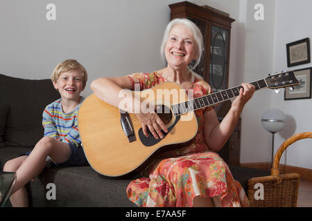 Ritratto di ragazzo seduto con la nonna a suonare la chitarra sul divano di casa Foto Stock