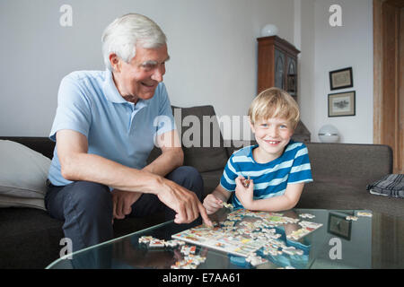 Ritratto di felice ragazzo risolvendo puzzle con il nonno nel salotto di casa Foto Stock