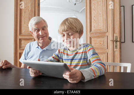 Senior un uomo guarda il nipote utilizzando tavoletta digitale in casa Foto Stock