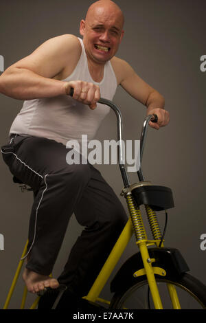 Ritratto di determinato uomo che lavora sulla cyclette contro uno sfondo grigio Foto Stock