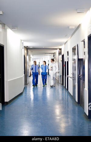 Tre i professionisti medici camminando insieme lungo un corridoio in un ospedale Foto Stock