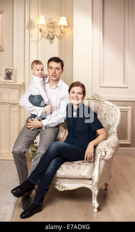 Giovane famiglia felice con un bambino in poltrona in salotto Foto Stock