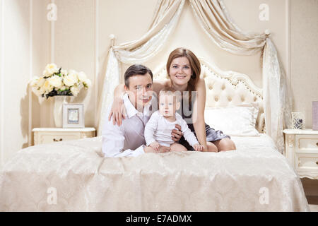 Giovane famiglia felice con un bambino su letto di casa Foto Stock