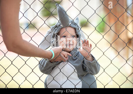 Carino piccolo ragazzo vestito in costume dell'elefante giocando dietro il net, vista ritagliata della madre in primo piano Foto Stock