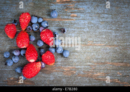 Fragole di bosco e mirtilli sul vecchio blu sullo sfondo di legno con spazio di copia Foto Stock