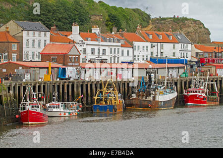 Coloratissime barche di pescatori ormeggiate nel porto di Whitby con edifici di inglese vacanza mare città clustered lungo la banchina Foto Stock