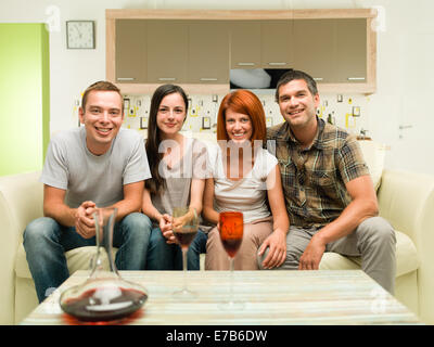 Happy amici seduti sul divano guardando film di commedia e bere il vino Foto Stock