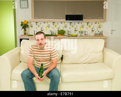 Vista frontale del uomo caucasico seduta sul lettino tenendo bottiglia di birra nelle sue mani, cercando stanco Foto Stock