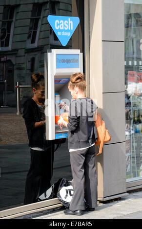 Donna che utilizza un bancomat al di fuori di un ramo di co-banca operativa Foto Stock